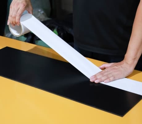 ゴムシートに両面テープを貼り付けている作業風景。剥離紙付きのオプション加工。